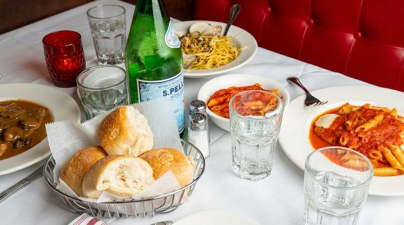 Table set with Italian dishes, including pasta, bread, and a bottle of San Pellegrino.