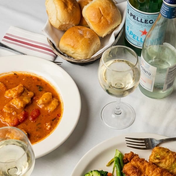 Table set with Italian dishes, including gnocchi in tomato sauce, fried chicken, bread, and wine.