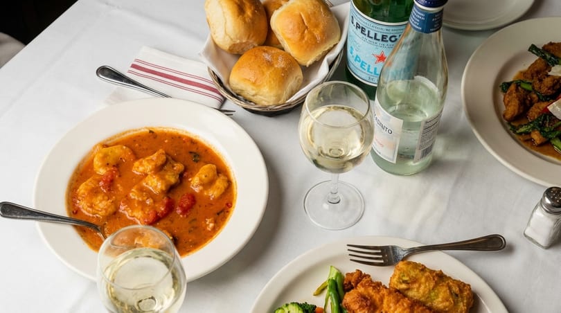 Table set with Italian dishes, including gnocchi in tomato sauce, fried chicken, bread, and wine.