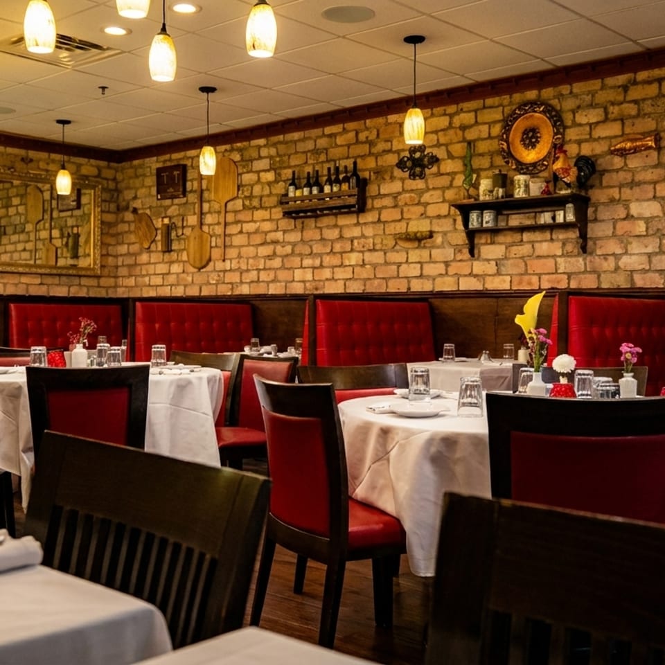 An empty Italian restaurant dining room with brick walls, red booths, and white-clothed tables.